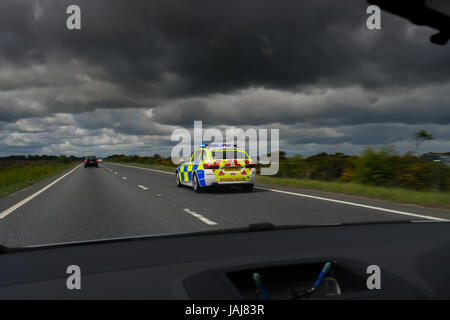 Una vettura della polizia di BMW accelera lungo una carreggiata del duello sopra una chiamata a un'emergenza con le luci si illuminano da all'interno di un'auto Foto Stock