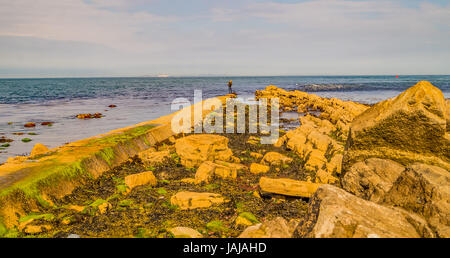 Un pescatore solitario si trova alla fine di un lungo passaggio pedonale sul bordo dell'acqua, Swanage, Dorset. Foto Stock