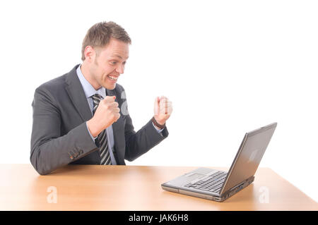 Junger Geschäftsmann in Anzug und Krawatte sitzt am Schreibtisch und arbeitet begeistet un Notebook seinem-PC. Vor Freigestellt weißem Hintergrund Foto Stock