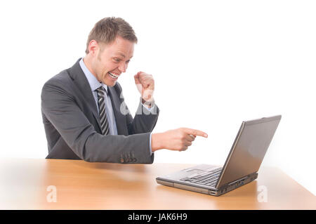 Junger Geschäftsmann in Anzug und Krawatte sitzt am Schreibtisch und arbeitet begeistet un Notebook seinem-PC. Vor Freigestellt weißem Hintergrund Foto Stock