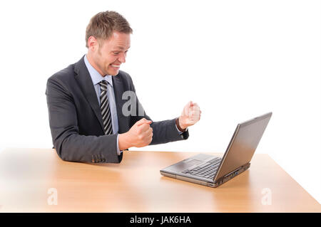 Junger Geschäftsmann in Anzug und Krawatte sitzt am Schreibtisch und arbeitet begeistet un Notebook seinem-PC. Vor Freigestellt weißem Hintergrund Foto Stock