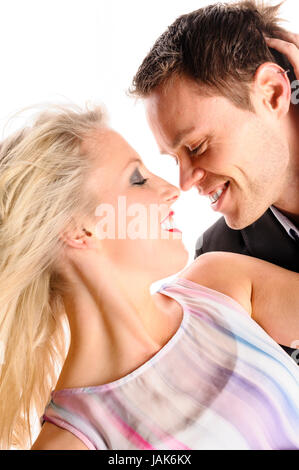 Ein junger Mann im dunklen Anzug und eine attraktive blonde Frau stehen vor freigestellt weißem Hintergrund, sie umarmen und küssen sich. Foto Stock