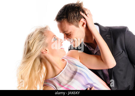 Ein junger Mann im dunklen Anzug und eine attraktive blonde Frau stehen vor freigestellt weißem Hintergrund, sie umarmen und küssen sich. Foto Stock