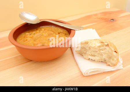 Cucchiaio appoggiato su di una ciotola di zuppa, con la metà di un pane su un tovagliolo Foto Stock