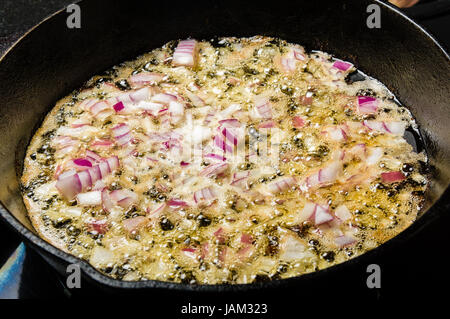 Carmelizing tagliare cipolle rosse in una padella in ghisa Foto Stock