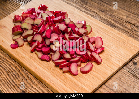 Tagliata a cubetti o trito di pezzi di rabarbaro rosso essendo preparato per la cottura Foto Stock