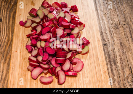 Tagliata a cubetti o trito di pezzi di rabarbaro rosso essendo preparato per la cottura Foto Stock