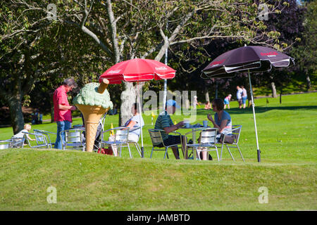 Persone Adulti rilassarsi al sole seduti su metallo cafe sedie bere accanto al grande gigante verde menta cono gelato con scaglie di cioccolato, la zappa, Foto Stock