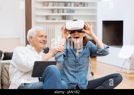 Coppia matura con tavoletta digitale e realtà virtuale auricolare in salotto Foto Stock