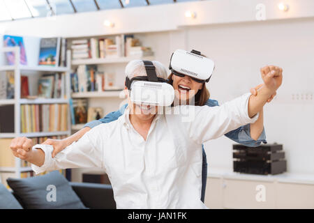 Coppia matura utilizzando la realtà virtuale auricolare in salotto Foto Stock