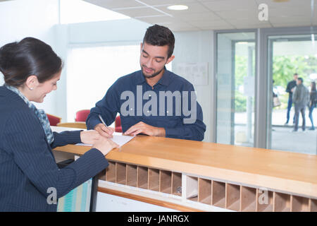 Ospiti di sesso maschile di riempire un formulario a hotel counter Foto Stock