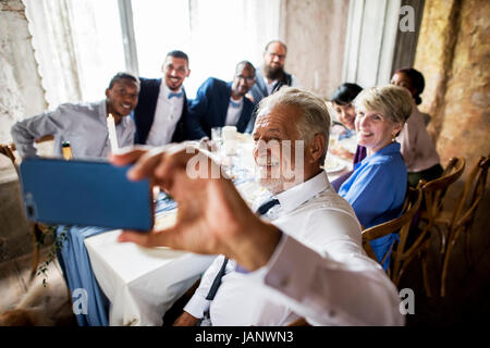 Gruppo di diversi amici prendendo selfie insieme al ricevimento di nozze Foto Stock