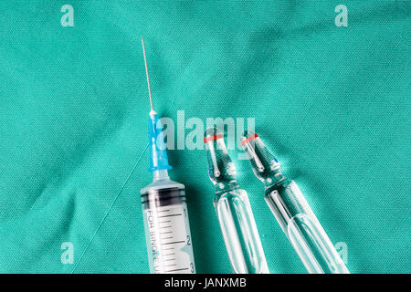 Siringa medica e fiale giacente sull'ospedale sfondo verde. Lo sfondo può essere una parte di tessili di un medico o un infermiere uniforme di lavoro Foto Stock