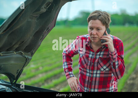 Donna che chiama riparazione auto da strada di campagna, femmina adulta persona in piedi dal veicolo rotto in campagna Foto Stock
