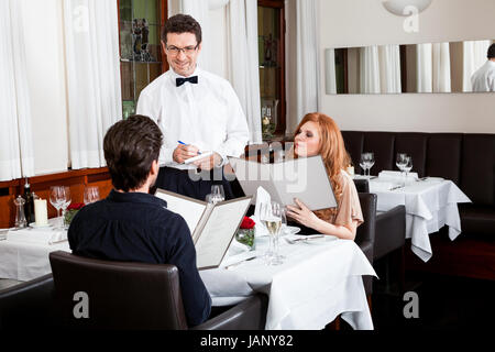 Frau und Mann beim Abendessen im Restaurant Kellner nimmt Bestellung auf Foto Stock