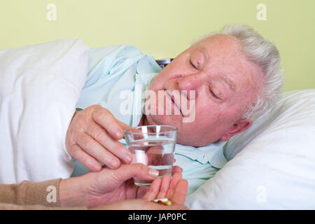 Immagine di un vecchio e malato uomo nel letto, il suo caregiver dandogli la medicina Foto Stock