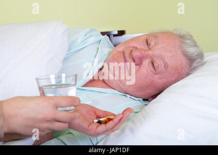 Immagine di un vecchio e malato uomo nel letto, il suo caregiver dandogli la medicina Foto Stock