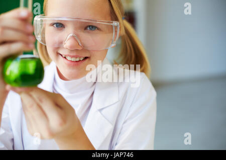Ritratto di carino schoolgirl tubo di contenimento con il liquido chimico e guardando la fotocamera Foto Stock