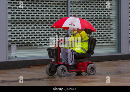 Fishergate, Preston, Lancashire, Regno Unito. 8 Giugno, 2017. Regno Unito Meteo. Gales & Heavy Rain in città. Senior, pensionato disabile utilizzando la mobilità scooter come acquazzoni torrenziali rendono difficile per gli acquirenti che lottano con le forti raffiche di vento, blustery e condizioni ventose. La previsione è per continuare la persistente e spesso heavy rain lentamente evolvendo verso est con forti venti. Credito: MediaWorldImages/Alamy Live News Foto Stock