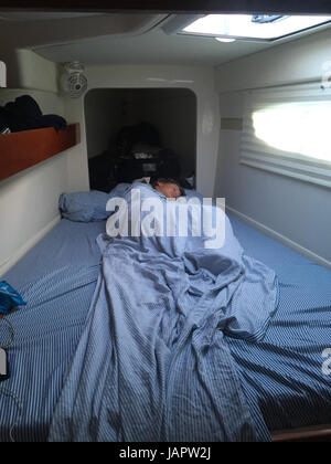 Giovane marinaio bambino addormentato in avanti la cabina di un pontone catamarano a vela Foto Stock