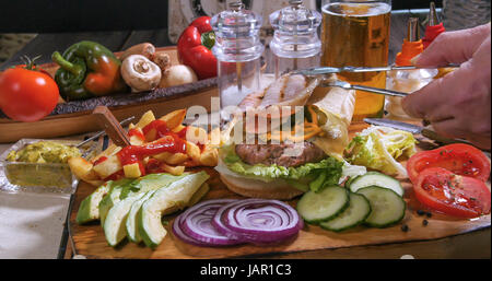 Aggiunta di bacon croccante su una deliziosa cheesburger con birra e patatine fritte Foto Stock