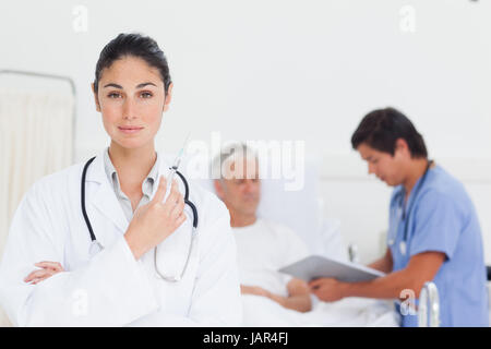 Medico grave guardando avanti tenendo in mano una siringa come lei a stare di fronte ad un tirocinante e di un paziente Foto Stock