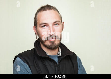 Close-up studio Ritratto di giovane sorridente barbuto uomo asiatico al di sopra di luce verde sullo sfondo della parete Foto Stock