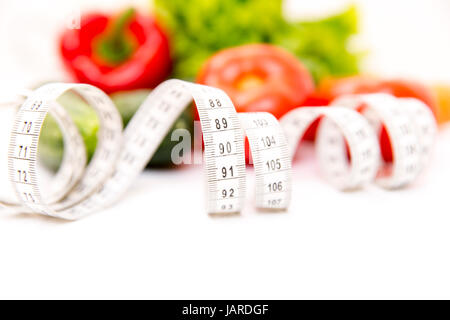 Fitness e una sana dieta alimentare concetto. Verdure fresche a foglia verde, nastro di misurazione isolata su sfondo bianco. Primo piano Foto Stock