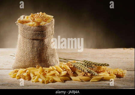 Sacco di iuta con varietà di pasta cruda sul tavolo di legno Foto Stock