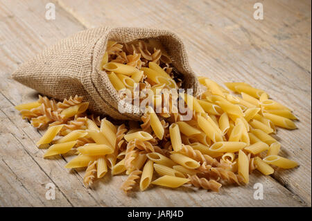 Sacco di iuta con varietà di pasta cruda sul tavolo di legno Foto Stock