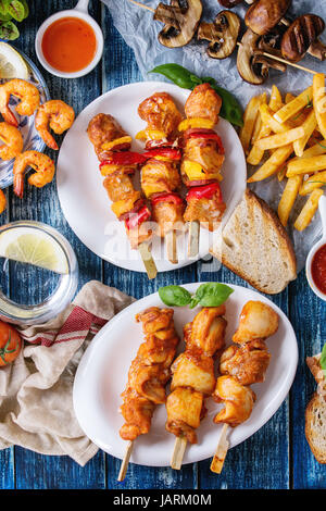 Varietà di snack barbecue il pranzo. Lastre grigliate di piccante spiedini di gamberi, pollo, maiale, verdure e funghi spiedini, pane, patate fritte patate con salse Foto Stock