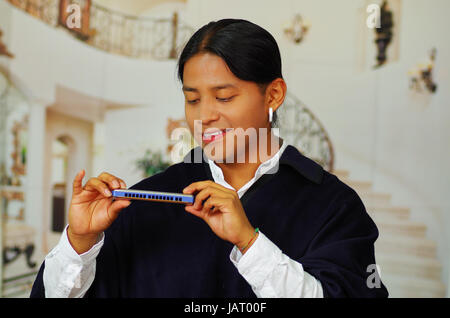 Close up ritratto del bel giovane uomo indigeno di Otavalo, Ecuador, giocando l'armonica Foto Stock