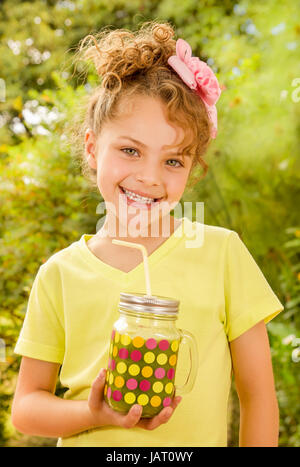 Giovane e bella ragazza che indossa un giallo t-shirt, tenendo un frullato sano bevanda fatta di super foods, frutta, bacche. Foto Stock