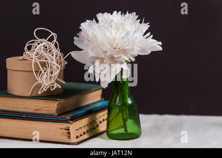 Vetreria Vintage accanto a vecchi libri con una peonia fiore Foto Stock