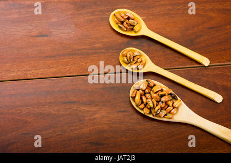 Cucchiai di legno con mais tostato in grani, noto come tostado in sud america, sparsi intorno al recipiente contenente salsa gialla, visto da sopra. Foto Stock