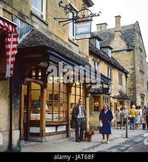 Broadway, England, Regno Unito - Giugno 1980: i visitatori e residenti nella parte anteriore del negozio di macellaio vicino a Lygon Arms Hotel in Cotswolds Foto Stock