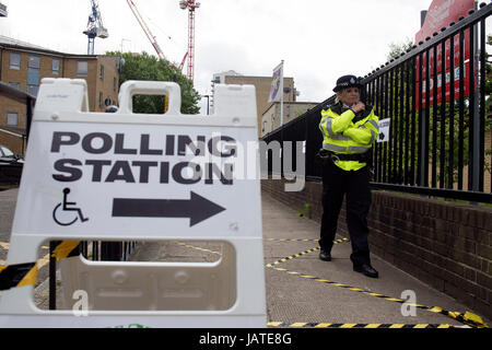 Un funzionario di polizia è di stanza al di fuori di un seggio a San Salvatore Scuola in legno di pioppo, Londra, come persone il loro voto nelle elezioni generali. Foto Stock