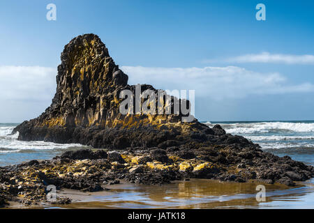 Una formazione di grande roccia sulla spiaggia risplende con il colore della luce riflessa fuori dell'acqua sottostante. Foto Stock