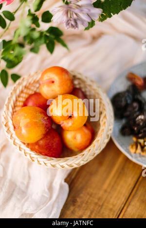 Vita sana, nutrizione, dieta alimentare, concetto di paese - close-up di rosso-giallo albicocche giacente nel cesto di paglia sulla neve di drappeggio bianco sul tavolo di legno Foto Stock