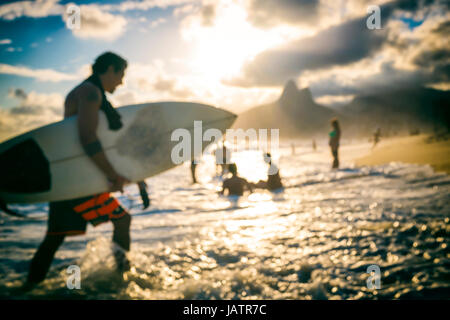 Sfocato suggestivo tramonto scena di un surfista sulla spiaggia di Ipanema con due fratelli montagne sullo sfondo Foto Stock