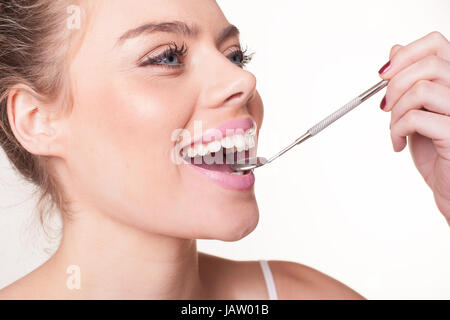 Donna attraente con splendidi denti bianchi tenendo un piccolo specchio dentale nella sua bocca per visualizzare i suoi denti Foto Stock