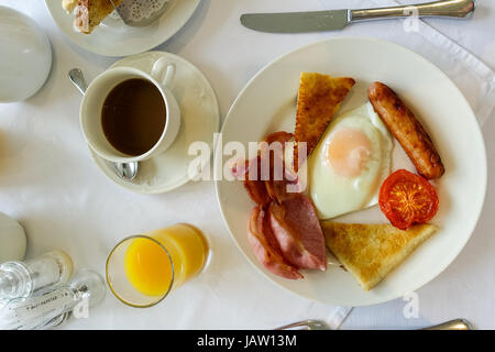 Ulster fry, colazione completa inclusa uovo fritto, fette di bacon, pomodoro, salsiccia, soda pane e pane di patate. Succo d'arancia e caffè per bere. Foto Stock