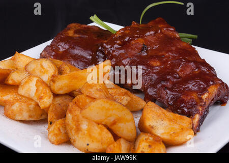 Close up BBQ Ribs con spicchi di patate su una piastra bianca. Foto Stock