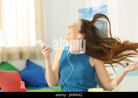 Teen ascoltare musica e ballare tenendo un telefono intelligente con i suoi capelli in movimento nella sua camera da letto Foto Stock