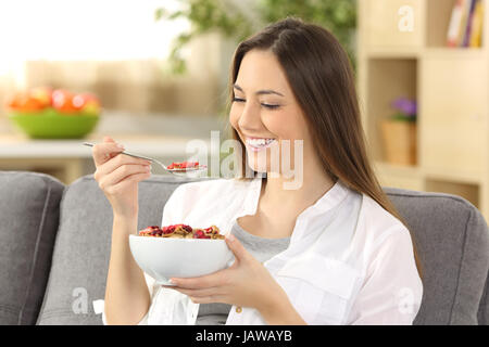 Donna allegra mangiare cereali seduto su un divano nel soggiorno di casa Foto Stock