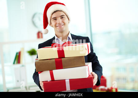 Immagine dell uomo d affari in Santa cappuccio con pila di giftboxes guardando la fotocamera con un sorriso Foto Stock