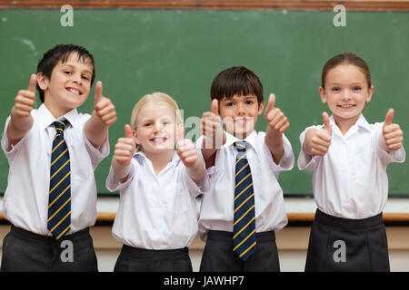 Scolari in uniformi di scuola dando pollice in alto Foto Stock