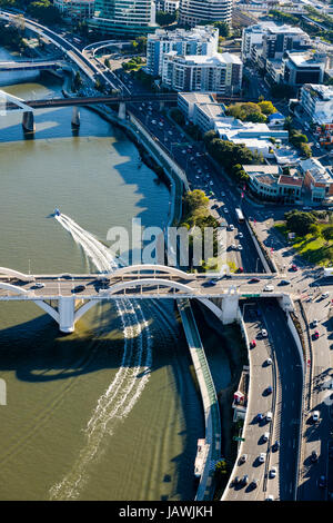 Un motoscafo passa al disotto di un ponte sul fiume lasciando il traffico su una superstrada dietro. Foto Stock