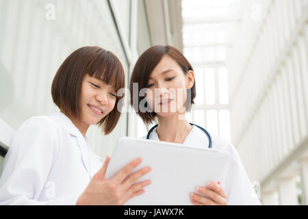 Asian medici aventi discussione al corridoio dell'ospedale. Utilizzando computer digitale compressa. Foto Stock