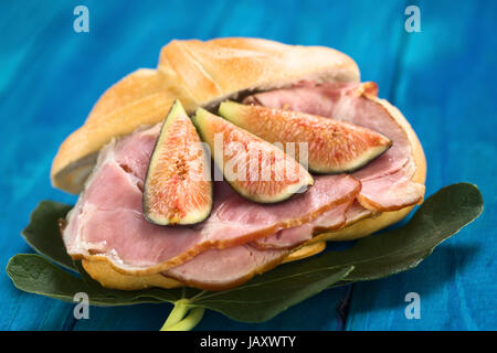 La figura freschi fette di prosciutto affumicato panino sulle foglie di fico su legno blu (messa a fuoco selettiva, Focus sul medio delle due fette di figura sulla sinistra) Foto Stock